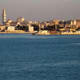 Sulla nostra sinistra appare lo skyline del centro storico di Bari, che sembra quasi galleggiare sul mare calmo e blu. In primo piano scorgiamo l�ottocentesco faro borbonico, mentre alle sue spalle si mostrano i massicci torrioni del Castello e la Cattedrale, con il suo alto campanile